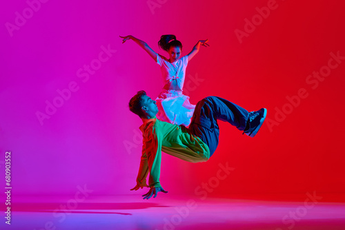 Expressive performance. Young man and woman, talented dancers in motion, dancing hip hop against pink red background in neon. Concept of hobby, action, street style, contemporary dance, youth, fashion © master1305