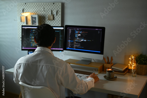 Focused male programmer working with coded data on computer screen at dark room