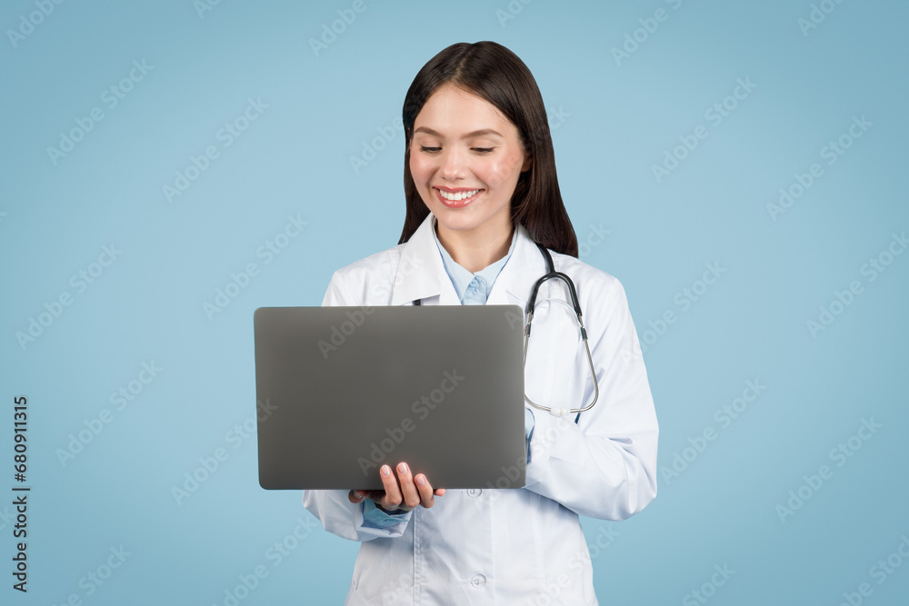 Happy female doctor with laptop on blue background Happy female doctor with laptop on blue background