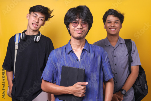 Portrait of three male college students in casual wear over yellow background