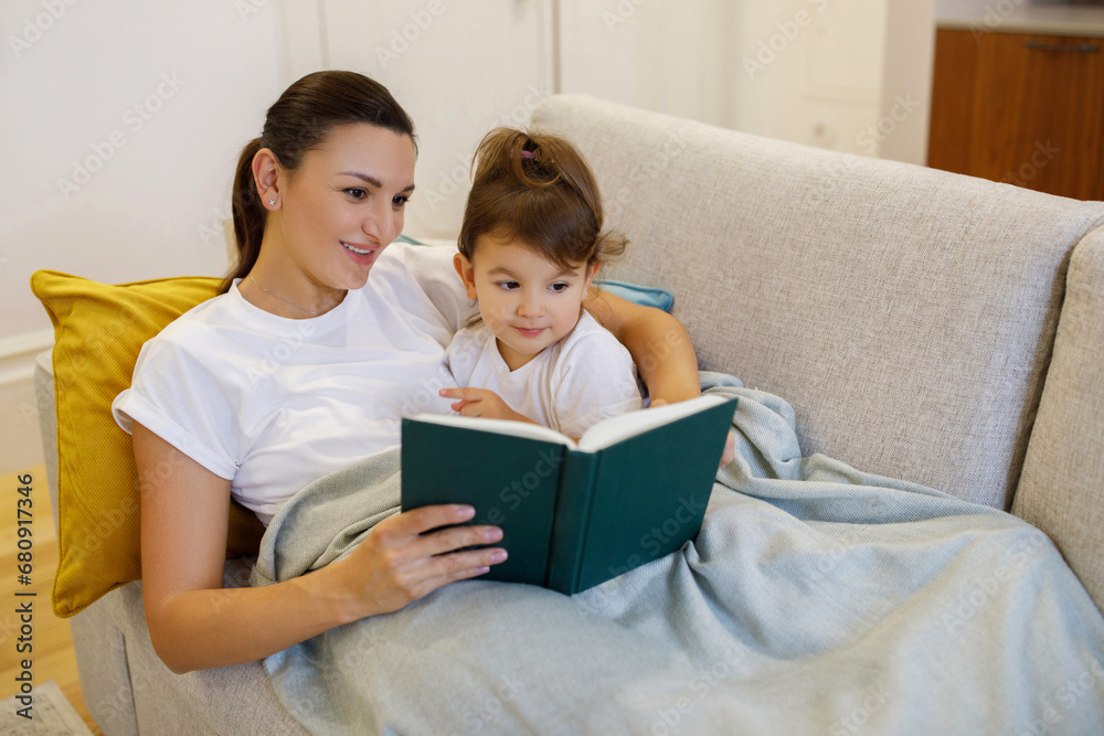 Loving Mother Reading Book To Her Cute Toddler Daughter At Home Loving Mother Reading Book To Her Cute Toddler Daughter At Home
