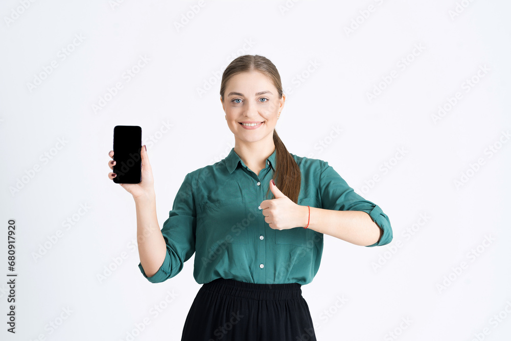 Attractive young woman shows an empty mobile phone display, recommends a cool application, approves and shows a thumb up isolated on a white studio background. Copy space, advertising Attractive young woman shows an empty mobile phone display, recommends a cool application, approves and shows a thumb up isolated on a white studio background. Copy space, advertising
