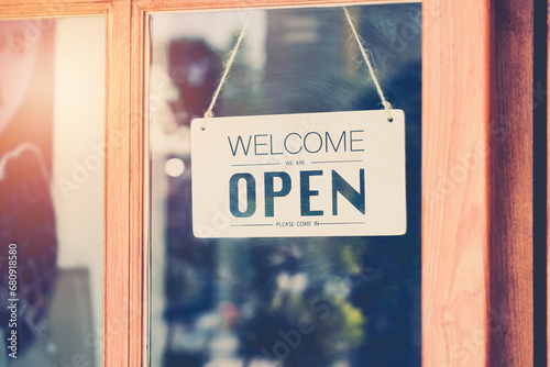 Welcome we're open word on wooden signboard behind transparent mirror door , vintage retro sign in front of cafe or restaurant photo