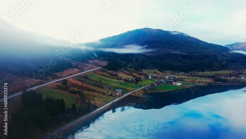 Drone View of Majestic Mountains, Fjord, and Waterfall with Green Trees and Soft Clouds Adding to the Scenic Beauty