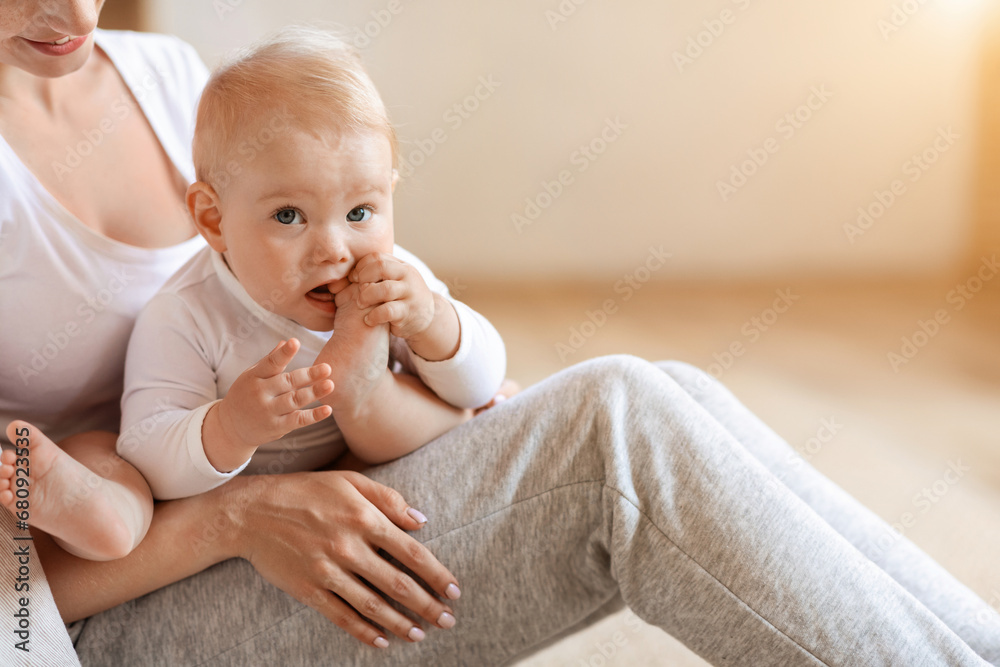 Adorable infant baby boy sitting in mother arms, chewing feet Adorable infant baby boy sitting in mother arms, chewing feet