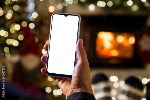 Fotografija Unrecognizable Man Hands Using smartphone by fireplace at home, white blank empty screen display