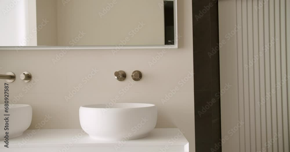 Modern bathroom with minimalist interior, ceramic washbowl, chrome water tap and mirror. Wall mounted faucet with concealed system. Contemporary clean public lavatory with wash basins Modern bathroom with minimalist interior, ceramic washbowl, chrome water tap and mirror. Wall mounted faucet with concealed system. Contemporary clean public lavatory with wash basins