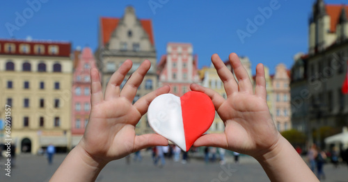 A red-white heart in the colors of the national flag of Poland in the hands of a child against the backdrop of the old town square. Independence Day of Poland. Freedom and Democracy photo