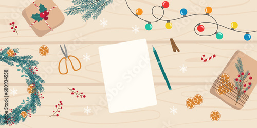 Christmas preparation top view background. Christmas decorations, garland and white blank sheet for writing a list, wishes, card, letter on light wooden table. Template for holiday design