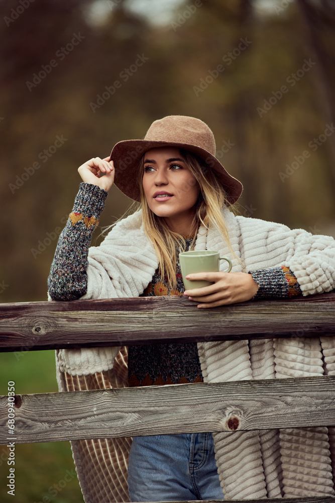 Obraz premium Fashionable girl, posing for the camera in nature, looking away, holding a cup of coffee.