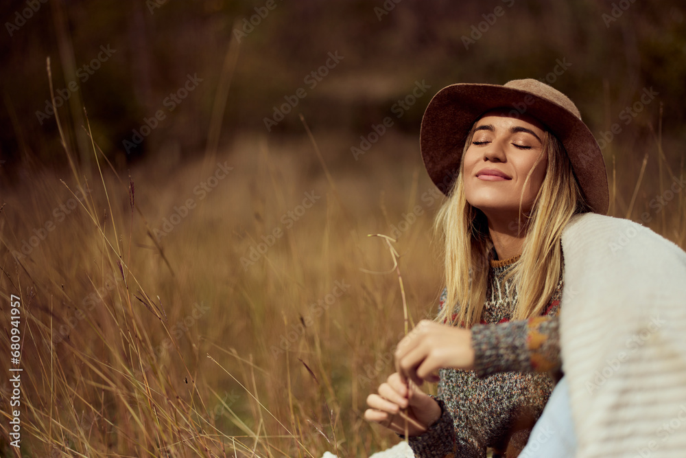 A smiling adult woman, enjoying herself outdoors, sitting in the field.