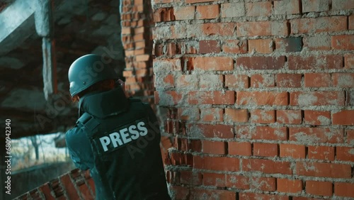 Brave female war journalist with a camera hides behind a wall during an open war military attack trying to take a picture for reporting on the war scene. Reporting live from war zone photo