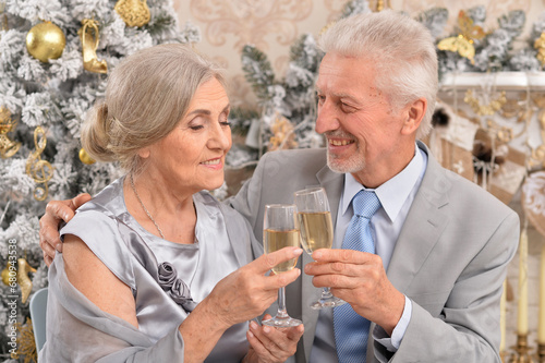 Old couple with champagne celebrating Christmas near tree