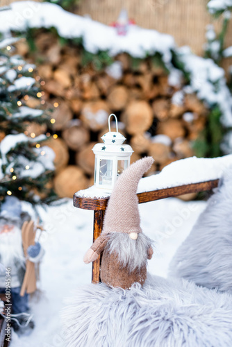 Soft toy gnome on snowy wooden chair with flashlight, outdoor backyard decor..