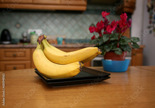 A bunch of bananas lying on a solid kitchen table. Sweet ripe bananas with yellow skin. Kitchen Scene with Bananas and Mixed Fruits Hand of ripe bananas in kitchen countertop