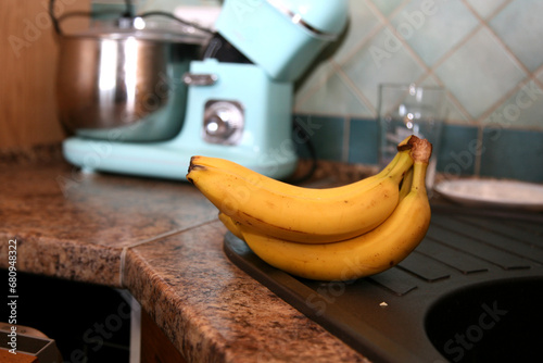 A bunch of bananas lying on a solid kitchen table. Sweet ripe bananas with yellow skin. Kitchen Scene with Bananas and Mixed Fruits Hand of ripe bananas in kitchen countertop