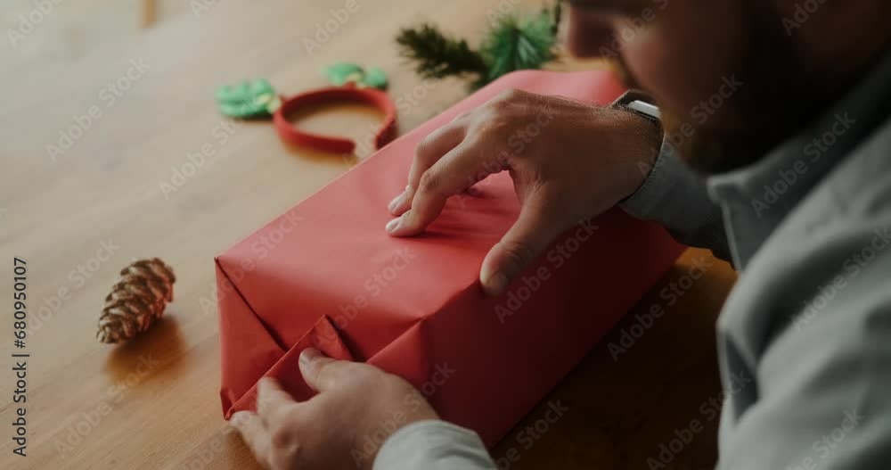 Close up of a man's hands wrapping gifts for Christmas and New Year. Wrapping paper and ribbons on the table for gift wrapping. Preparation for Christmas celebration, gifts for family and friends.