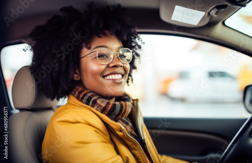 smiling african american young woman driving car in urban city environment wearing glasses