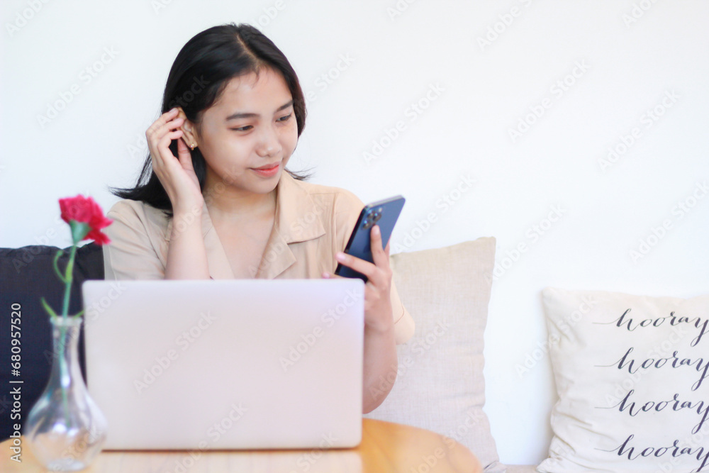 happy asian woman sitting on cozy sofa using smartphone with laptop on wooden table wearing fashionable clothes, female online business owner working at home happy asian woman sitting on cozy sofa using smartphone with laptop on wooden table wearing fashionable clothes, female online business owner working at home