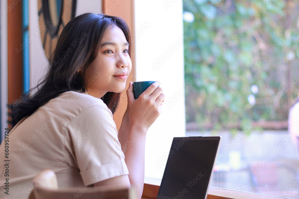 happy asian woman sitting in cafe drinkking coffee and working with laptop near window wearing fashionable clothes, contemplative female remote worker holding mug in coffee shop look away happy asian woman sitting in cafe drinkking coffee and working with laptop near window wearing fashionable clothes, contemplative female remote worker holding mug in coffee shop look away