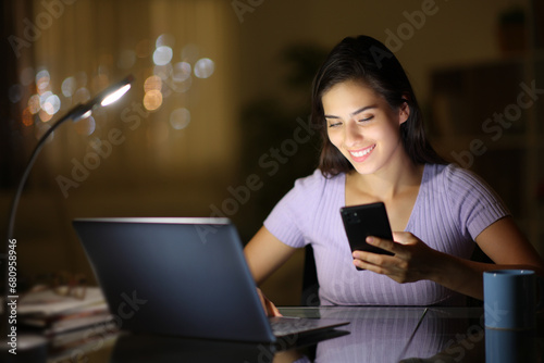 Happy woman using laptop and phone in the night at home