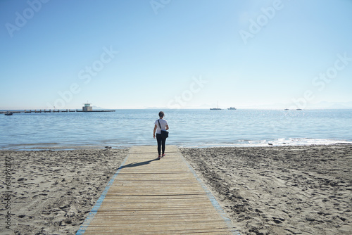Chica andado por una pasarela de madera que lleva al mar