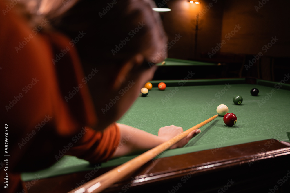 Woman with cue pointing at billiard ball at table. Playing billiards concept - obrazy, fototapety, plakaty 