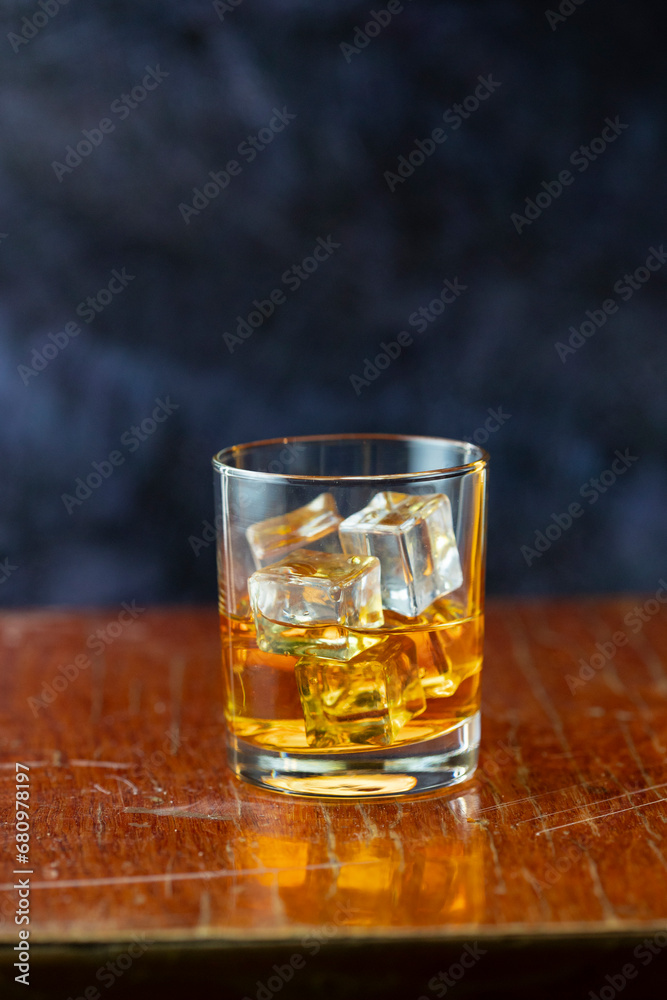 A glass of whiskey and ice old polished table on dark background A glass of whiskey and ice old polished table on dark background