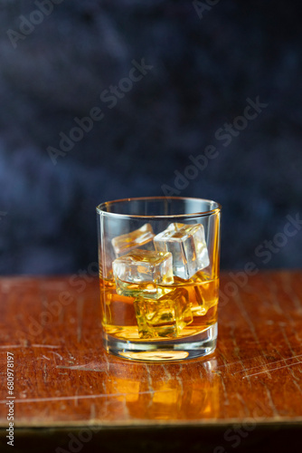 A glass of whiskey and ice old polished table on dark background