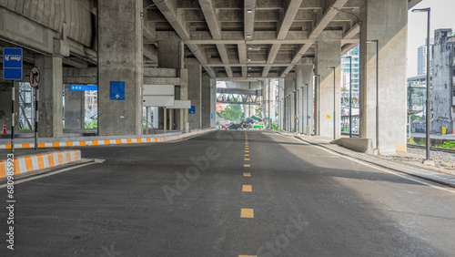 Roads in Thailand are under buildings. The side of the road is full of lamp posts. There are traffic signs pointing the way.