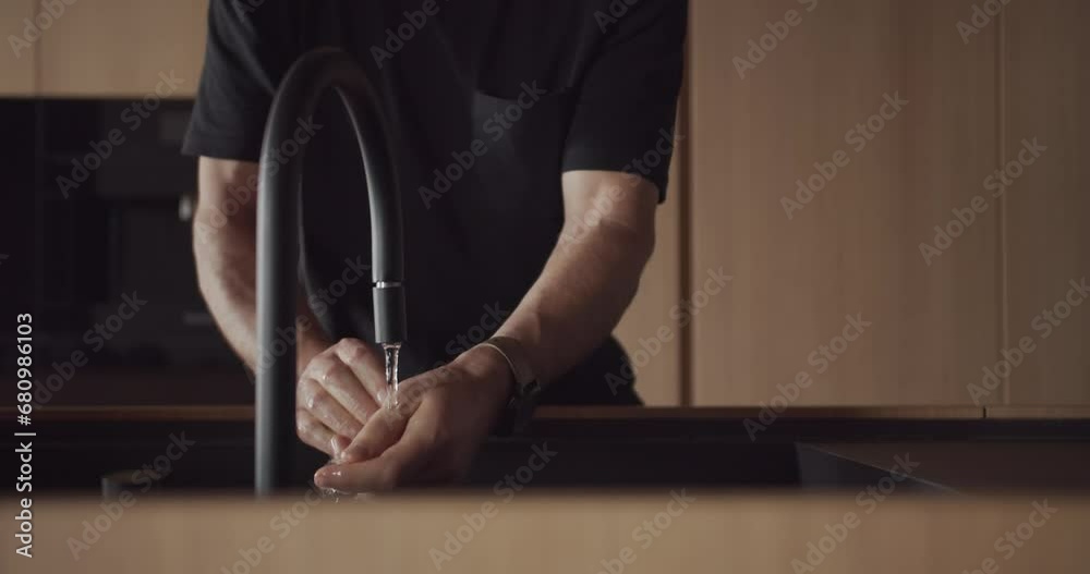 A man washes his hands at home in the modern kitchen interior. Contemporary modern and minimalist design apartment, Stylish interior of the luxury kitchen with italian design. Modern black faucet.