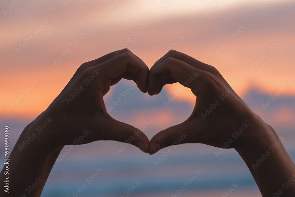 Hands forming a heart shape with sunset silhouette