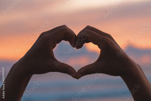 Hands forming a heart shape with sunset silhouette