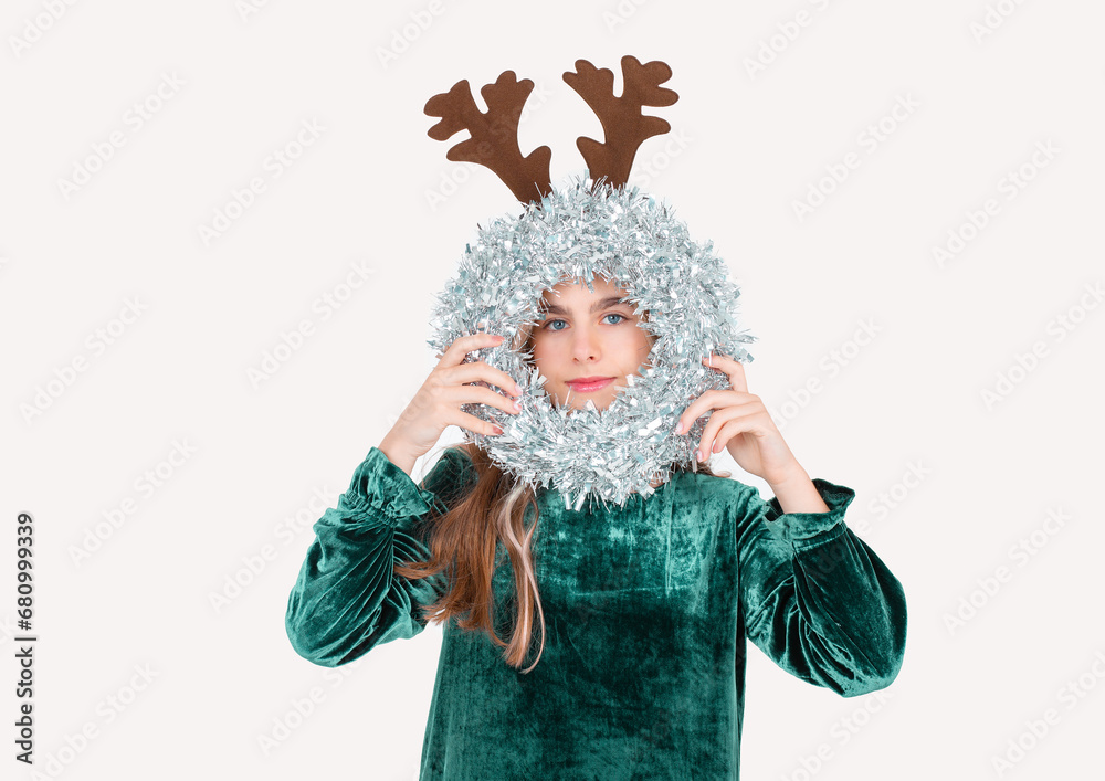 Festively dressed cute girl wearing reindeer antlers holding Christmas decorations on isolated white background