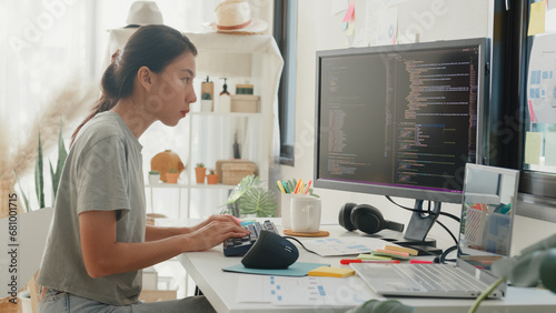 Side view of professional young Asia girl IT development programmer typing on keyboard coding programming fixing data code on computer screen and laptop on table in workroom at house office.