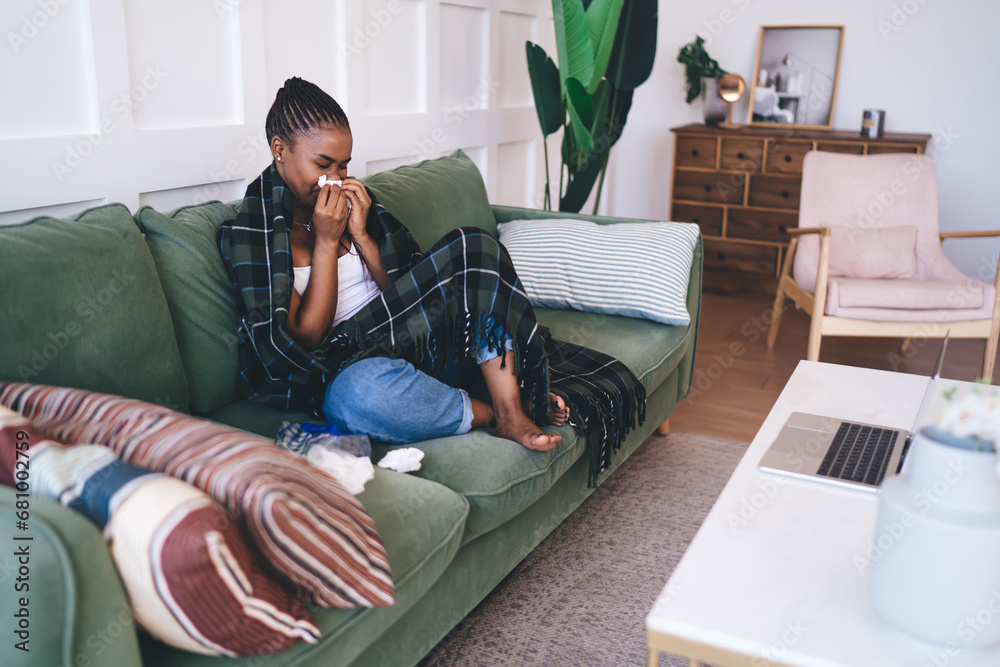 Obraz premium Ethnic unhealthy woman with tissue paper sitting on couch in living room
