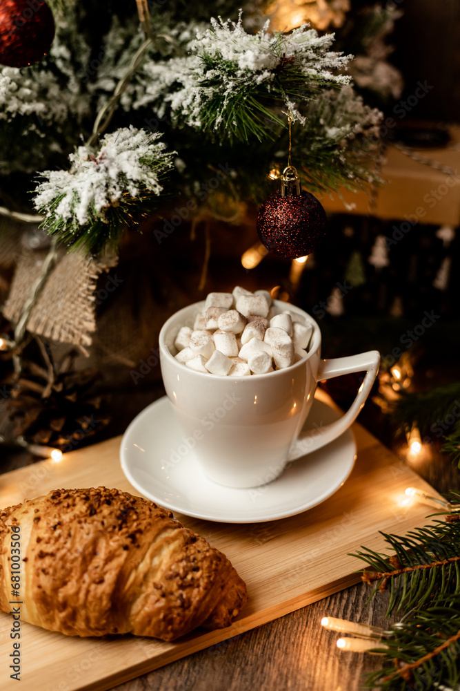 A marshmallow in a cup and croissant stand on the table near the Christmas tree A marshmallow in a cup and croissant stand on the table near the Christmas tree