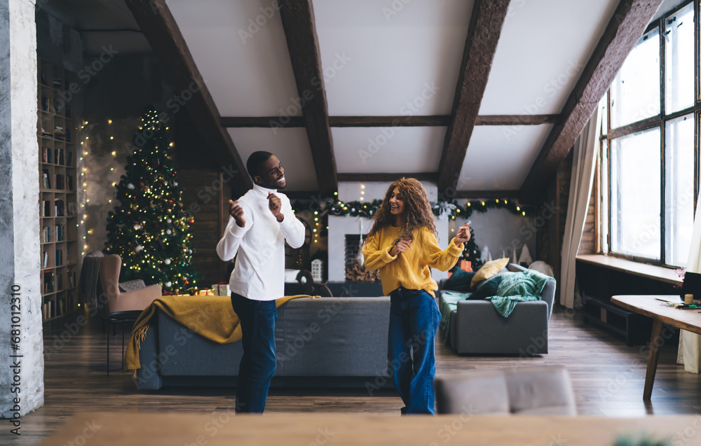 Joyful dance of Black man and woman in festive loft with Christmas tree. He shares dance step with her