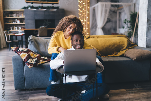 cheerful young Black man using a laptop with a joyous Black woman embracing him from behind