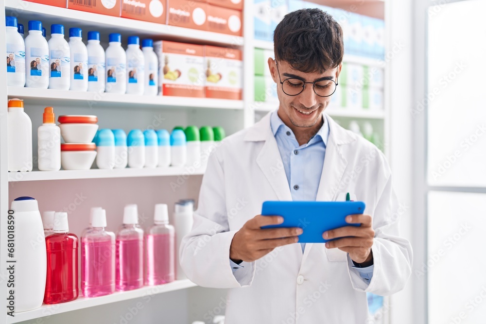 Young hispanic man pharmacist using touchpad working at pharmacy