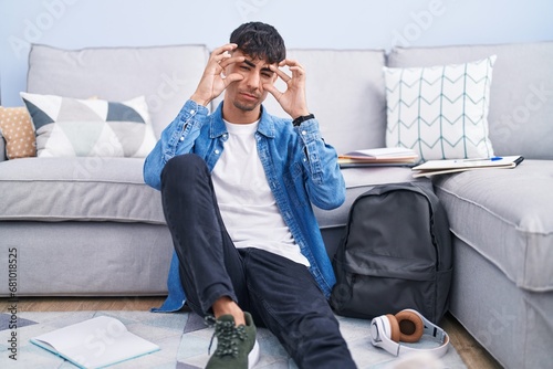 Young hispanic man sitting on the floor studying for university trying to open eyes with fingers, sleepy and tired for morning fatigue