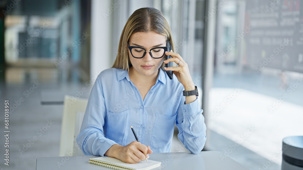 Young blonde woman business worker talking on smartphone taking notes at office Young blonde woman business worker talking on smartphone taking notes at office