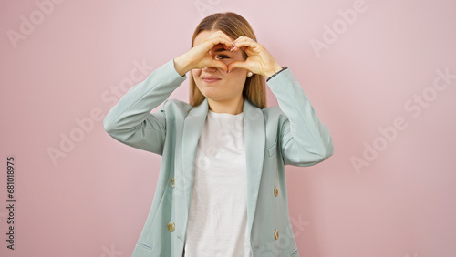 Young blonde woman business worker smiling confident doing heart gesture over isolated pink background