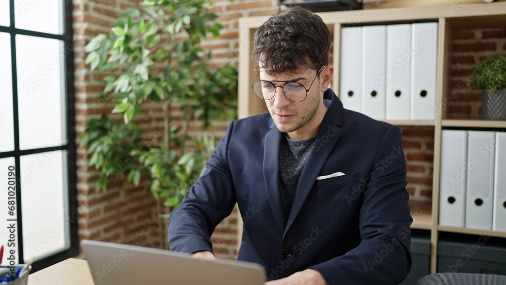 Young hispanic man business worker using laptop with serious face at office