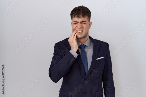 Young hispanic business man wearing suit and tie touching mouth with hand with painful expression because of toothache or dental illness on teeth. dentist