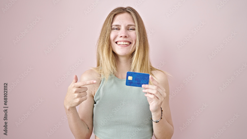 Young blonde woman smiling confident pointing to credit card over isolated pink background Young blonde woman smiling confident pointing to credit card over isolated pink background