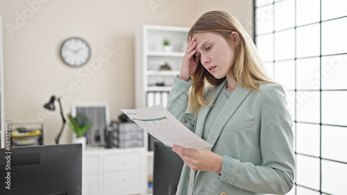 Young blonde woman business worker reading document with worried expression at office photo