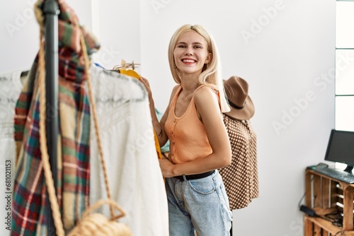 Young blonde woman customer choosing clothes smiling at clothing store
