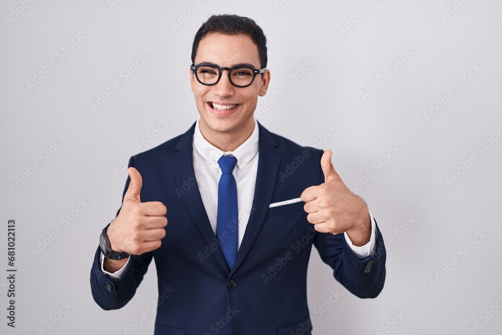 Young hispanic man wearing suit and tie success sign doing positive gesture with hand, thumbs up smiling and happy. cheerful expression and winner gesture. Young hispanic man wearing suit and tie success sign doing positive gesture with hand, thumbs up smiling and happy. cheerful expression and winner gesture.