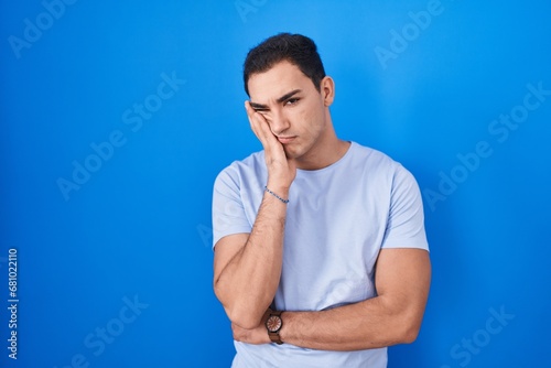Young hispanic man standing over blue background thinking looking tired and bored with depression problems with crossed arms.
